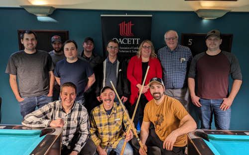 Group of people posing around a pool table with a sign for OACETT in the background.