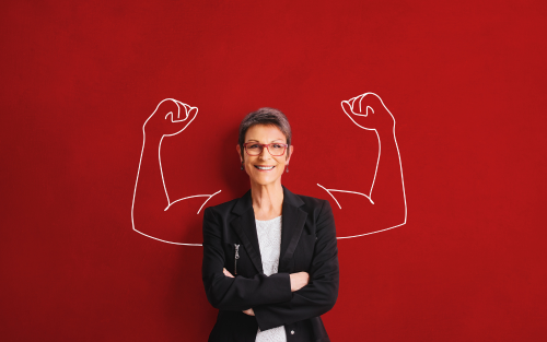 Smiling woman in a black blazer standing with arms crossed in front of a red background with drawn muscular arms behind her.