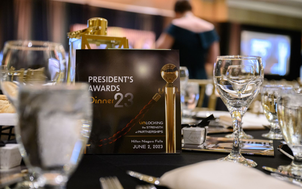 Table setting at the President's Awards Dinner 2023, with a sign detailing the event held on June 2, 2023, at Hilton Niagara Falls.