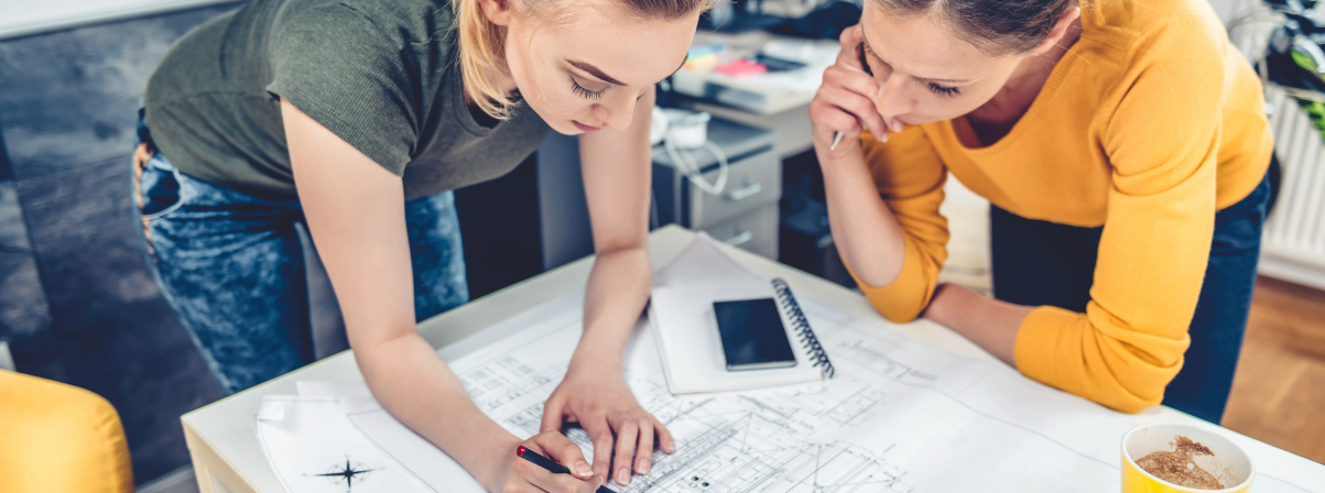 "Two women reviewing architectural plans on a table."