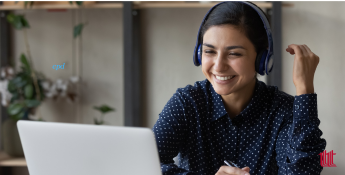 A woman wearing headphones and a dark polka-dotted shirt smiles while looking at her laptop screen. She appears to be engaged in an online conversation or meeting, with a relaxed and cheerful demeanor